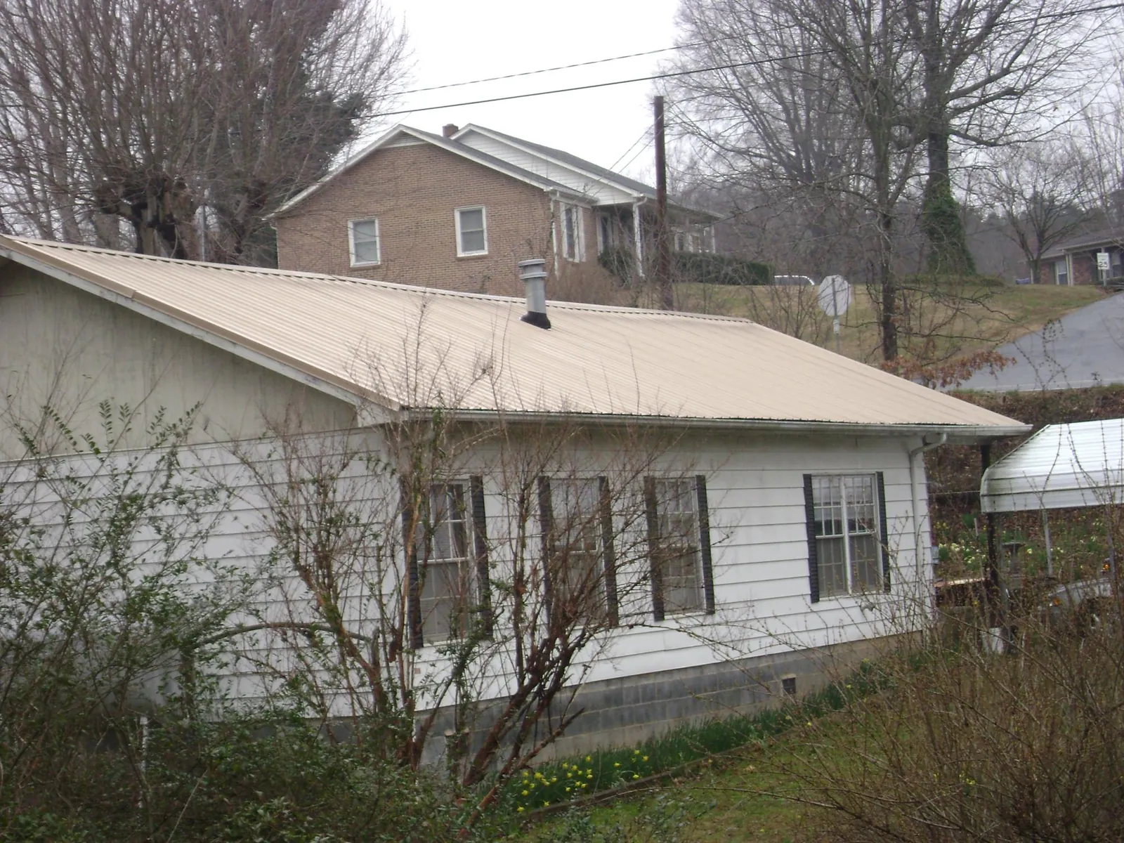 Tan metal roof on a white sided house set into a hillside — Commercial Roofing by Roofing Brothers in Springvale